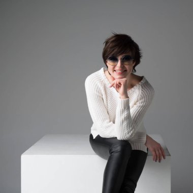 Çekici, siyah saçlı, güneş gözlüklü beyaz kız gri arka plandan kameraya bakıyor. Stüdyoda poz veren güzel bir kadın..