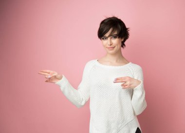 Çekici stil sahibi genç bir kadın fotokopi makinesini gösterip kameraya gülümsüyor. Tatlı kız yumuşak pembe arka planda bir şeyler sergiliyor..