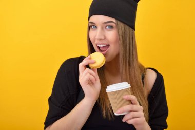 Hippi kız kek yer ve sarı arka planda kahve içer. Stüdyo kadın portresi, tatlı yemek ve sıcak içecek..