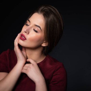Siyah arka planda çekici genç bir kadının portresi. Mükemmel makyajlı, zarif, koyu kırmızı bir elbise giyen harika bir kız. Güzellik ve moda