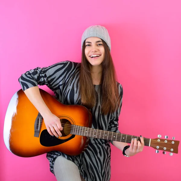 Young smiling woman playing music on acoustic guitar, over vivid pink background. Girl guitar player