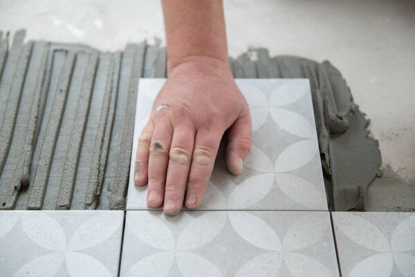 Тайлер кладет керамическую плитку на пол. Профессиональный работник делает ремонт. Строительство. Руки на плитку. Ремонт и строительство нового дома