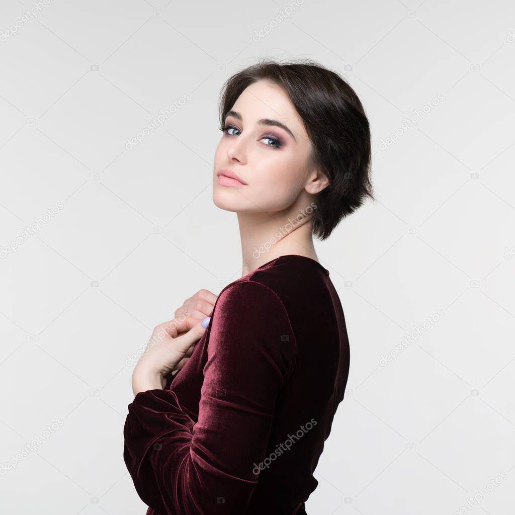 Beauty female portrait. Young attractive woman posing at studio. Beautiful model with perfect make-up dressed evening burgundy dress looking at camera.