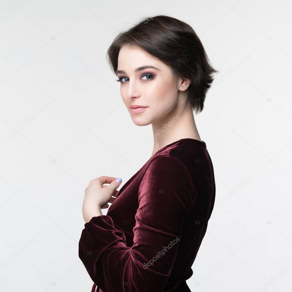 Beauty female portrait. Young attractive woman posing at studio. Beautiful model with perfect make-up dressed evening burgundy dress looking at camera.