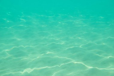 Suyun altında. Denizin dibinde güneş parıldıyor. Suyun altındaki dalgalar ve ışıldayan güneş ışınları. Derin turkuaz mavi deniz. Okyanus. Şeffaf su ve kumdaki ışık.