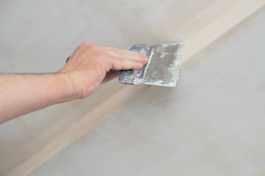 İşçi kokuşmuş alçıpan tavanı yeni binada. Tamirci sıva tahtasıyla çalışır, kuru taş duvar yapıştırır, ev dekorasyonu yapar. Evde tamirat yapan bir adam. Erkek elinde oyuncak bıçak.