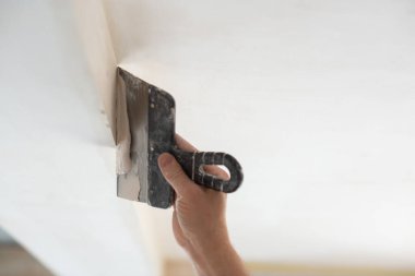 İşçi kokuşmuş alçıpan tavanı yeni binada. Tamirci sıva tahtasıyla çalışır, kuru taş duvar yapıştırır, ev dekorasyonu yapar. Evde tamirat yapan bir adam. Erkek elinde oyuncak bıçak.