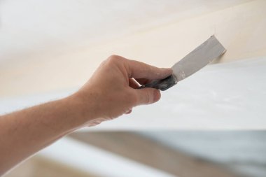 İşçi kokuşmuş alçıpan tavanı yeni binada. Tamirci sıva tahtasıyla çalışır, kuru taş duvar yapıştırır, ev dekorasyonu yapar. Evde tamirat yapan bir adam. Erkek elinde oyuncak bıçak.