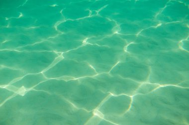 Suyun altında. Denizin dibinde güneş parıldıyor. Suyun altındaki dalgalar ve ışıldayan güneş ışınları. Derin turkuaz mavi deniz. Okyanus. Şeffaf su ve kumdaki ışık.