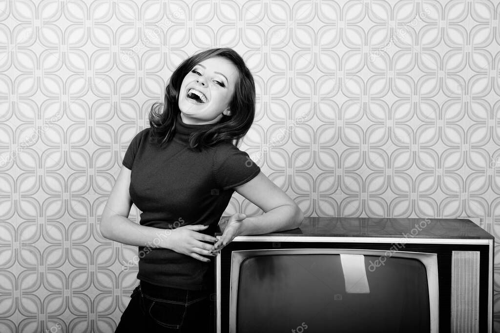 Young charming woman staing at room with vintage wallpaper and retro TV set, retro stylization 60-70s, black and white. Self isolation, quarantine, stay at home