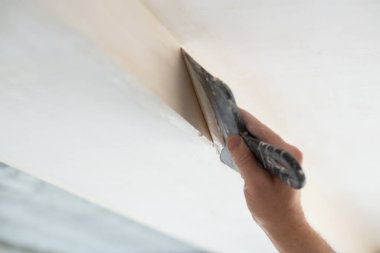 İşçi kokuşmuş alçıpan tavanı yeni binada. Tamirci sıva tahtasıyla çalışır, kuru taş duvar yapıştırır, ev dekorasyonu yapar. Evde tamirat yapan bir adam. Erkek elinde oyuncak bıçak.