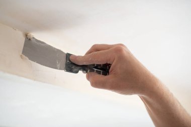 İşçi kokuşmuş alçıpan tavanı yeni binada. Tamirci sıva tahtasıyla çalışır, kuru taş duvar yapıştırır, ev dekorasyonu yapar. Evde tamirat yapan bir adam. Erkek elinde oyuncak bıçak.