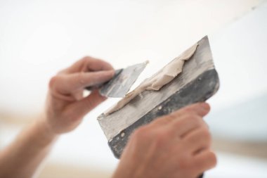 İşçi kokuşmuş alçıpan tavanı yeni binada. Tamirci sıva tahtasıyla çalışır, kuru taş duvar yapıştırır, ev dekorasyonu yapar. Evde tamirat yapan bir adam. Erkek elinde oyuncak bıçak.