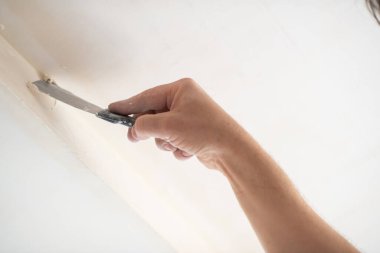 İşçi kokuşmuş alçıpan tavanı yeni binada. Tamirci sıva tahtasıyla çalışır, kuru taş duvar yapıştırır, ev dekorasyonu yapar. Evde tamirat yapan bir adam. Erkek elinde oyuncak bıçak.