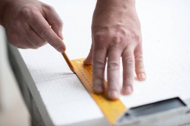 Köpük, yelken montajı. Bir adam köpük kesiyor. Isınıyor. Evde tamirat var. DIY onarımı. Polistiren köpükle çalışmak, duvarların ve tavanın yalıtımı. Aletleri yakın çekim olan erkek elleri