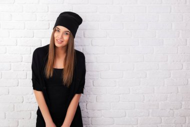 Siyah giyinmiş, beyaz tuğlaların üzerine çekilen genç ve neşeli bir kızın portresi.. 