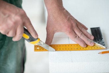 Köpük, yelken montajı. Bir adam köpük kesiyor. Isınıyor. Evde tamirat var. DIY onarımı. Polistiren köpükle çalışmak, duvarların ve tavanın yalıtımı