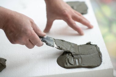 Tavana yapıştırmak için köpüğe macun bıçağı süren bir adam. Köpük, yelken montajı. Bir adam köpük yapıştırır. Tavan yalıtımı. Isınıyor. Evde tamirat var. Aletleri olan erkek eller. DIY onarımı