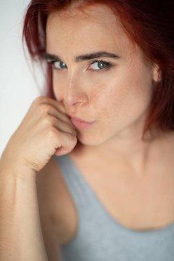 Güzel, genç, kızıl saçlı, çilli, mavi gözlü bir kadın. Evde poz veren, kameraya bakan, günlük kıyafetler giyen çekici bir kızın portresi.