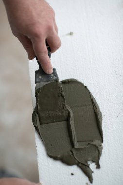 Tavana yapıştırmak için köpüğe macun bıçağı süren bir adam. Köpük, yelken montajı. Bir adam köpük yapıştırır. Tavan yalıtımı. Isınıyor. Evde tamirat var. Aletleri olan erkek eller. DIY onarımı