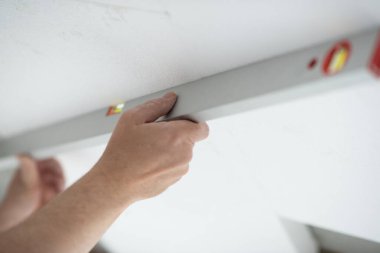 Erkeklerin elindeki alet seviyesi ve tavanın düz yatay yüzeyi. Köpük, yelken montajı. Adamın biri köpük tavan seviyesini kontrol ediyor. Tavan yalıtımı. Isınıyor. Evde tamirat var. DIY onarımı