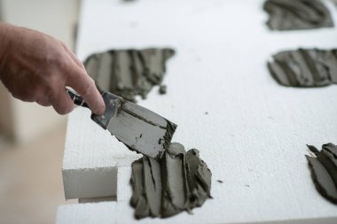 Tavana yapıştırmak için köpüğe macun bıçağı süren bir adam. Köpük, yelken montajı. Bir adam köpük yapıştırır. Tavan yalıtımı. Isınıyor. Evde tamirat var. Aletleri olan erkek eller. DIY onarımı