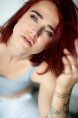 Mavi gözlü, güzel, genç, kızıl bir kadın. Evde poz veren, kameraya bakan, günlük kıyafetler giyen çekici bir kızın portresi.