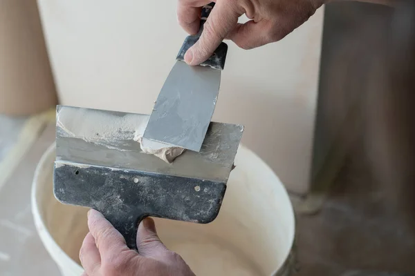 Worker putsty plasterboard ceiling in new building. Repairman works with plasterboard, plastering dry-stone wall, home improvement. A man makes repairs at home. Putty knife in male hand