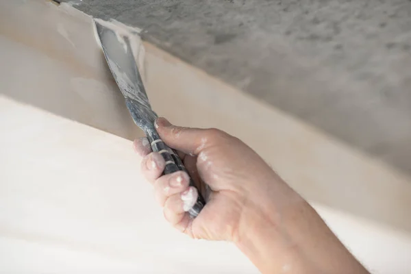 Worker putsty plasterboard ceiling in new appartment, bottom view. Repairman works with plasterboard, plastering dry-stone wall, home improvement. A man makes repairs at house. Putty knife in male hand. Hand work