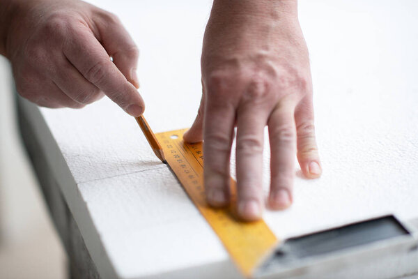 пенополистирол, герметизация монтажа. Человек режет пену. Потепление. Ремонт в доме. DIY ремонт. Работа с пенополистиролом, изоляция стен и потолка. Мужские руки с инструментами крупным планом