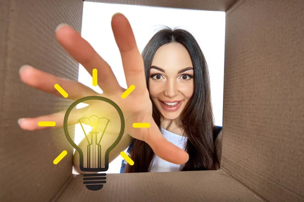 Happy girl opening postal package with light idea cartoon lamp inside. Excited young woman finds an idea bulb in cardboard box. Gift, present, delivery, shipment, sale, brilliant solution.