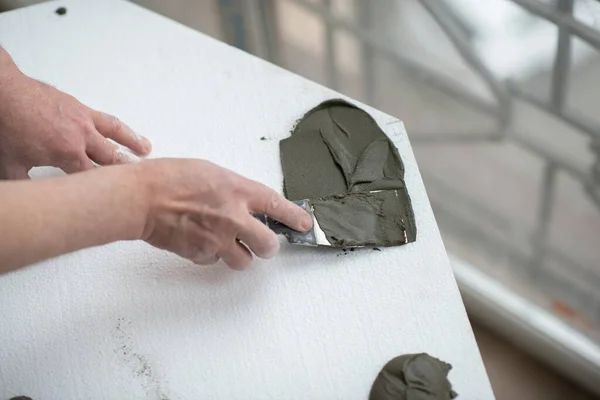 A man putsglue with putty knife on foam to stick it to the ceiling. Styrofoam, seiling mounting. A man glues foam. Ceiling insulation. Warming. Repair in the house. Male hands with tools. DIY repair