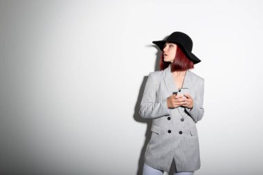 Akıllı telefon kullanan, beyaz yerine kapalı mekan portresi çizen şık bir kadın. Gri jaket giyen, siyah şapkalı, cep telefonunda mesajlaşan modern bir kız.