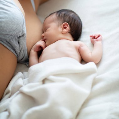 Evde yatağında annesinin göğüslerinin yanında yatan yeni doğmuş şirin bir bebek. Aile değerleri, anne bakımı, emzirme kavramı