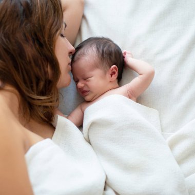 Anne yeni doğmuş kızıyla evde yatıyor, bebeğe bakıyor ve onu öpüyor. Aile değerleri, anne bakımı