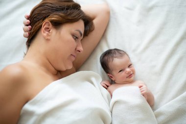 Anne evde yeni doğmuş kızıyla yatakta yatıyor, bebeğiyle ilgileniyor. Aile değerleri, anne bakımı