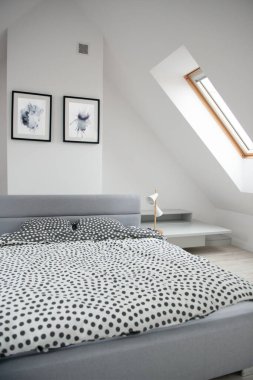 Mansard 'daki yatak odasının iç dekorasyonu, ahşap yatak ve zarif aksesuarlarla modern monokrom tasarımı. Duvarında soyut resimler olan şık bir ev dekoru.. 