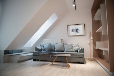 Mansard 'daki oturma odasının modern tasarımı. Koltuğu ve zarif aksesuarları var. Duvarında soyut resimler olan şık bir ev dekoru.. 