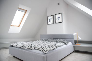 Mansard 'daki yatak odasının iç dekorasyonu, ahşap yatak ve zarif aksesuarlarla modern monokrom tasarımı. Duvarında soyut resimler olan şık bir ev dekoru.. 