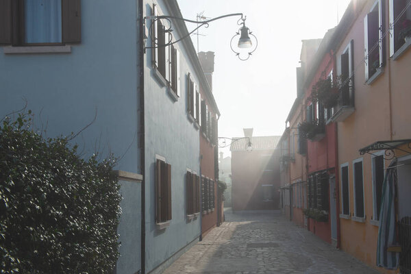 Misty picture of street with colored houses in fog, italian island Burano, province of Venice, Italy, foggy weather.