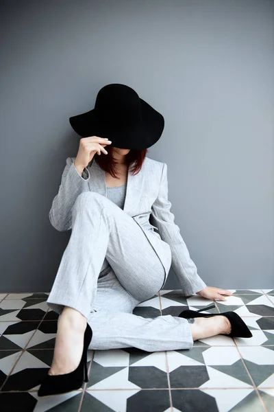 漂亮的时尚女人 身穿浅灰西服 头戴黑色帽子的女孩的全长肖像 在室内的深灰墙上摆姿势 — 图库照片