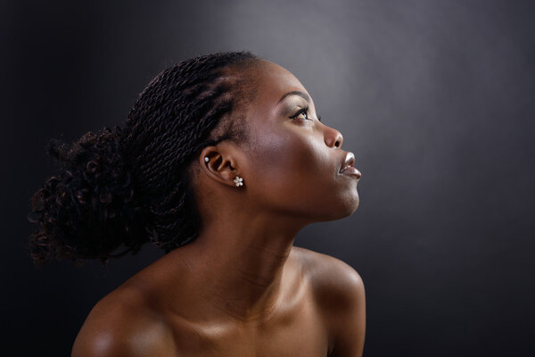 Beautiful young african woman looking up into the corner, face with hand portrait over dark background