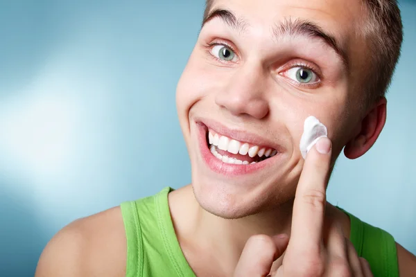 Joven hombre poniendo crema loción en la cara — Foto de Stock