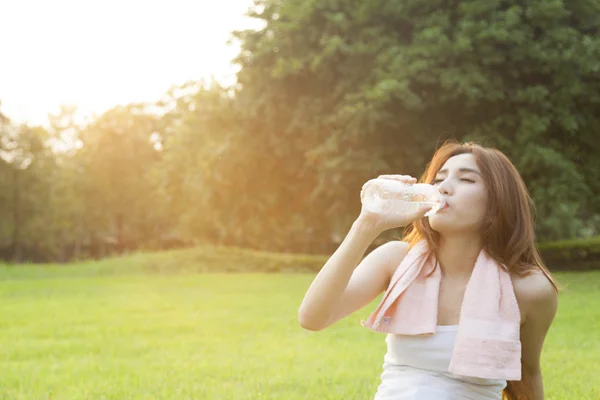 Kvinna dricksvatten och sitta på gräset. — Stockfoto