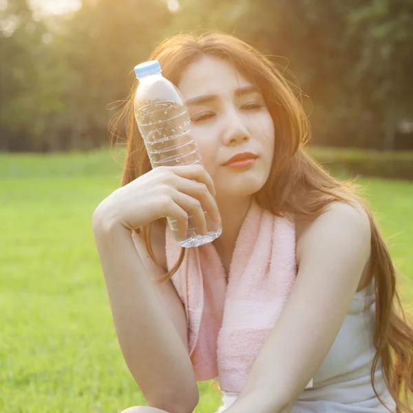 Kobieta siedzi i trzyma butelkę wody. — Zdjęcie stockowe