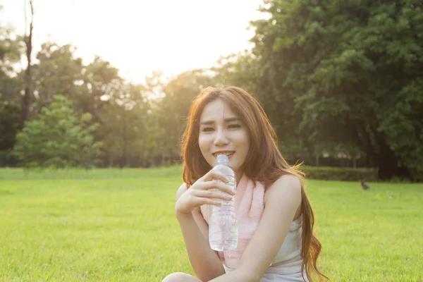 Vrouw drinkwater en zitten op gras. — Stockfoto