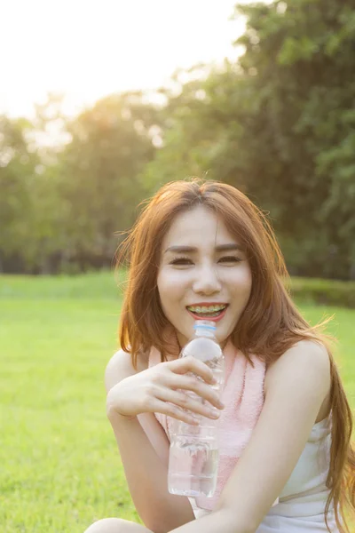 Vrouw drinkwater en zitten op gras. — Stockfoto