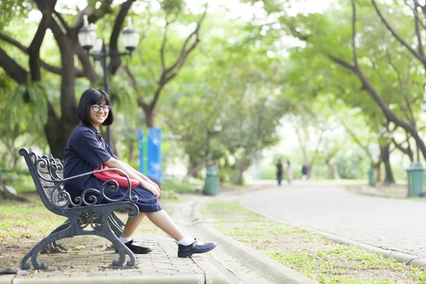Dívka, která nosí brýle sedí na lavičce. — Stock fotografie