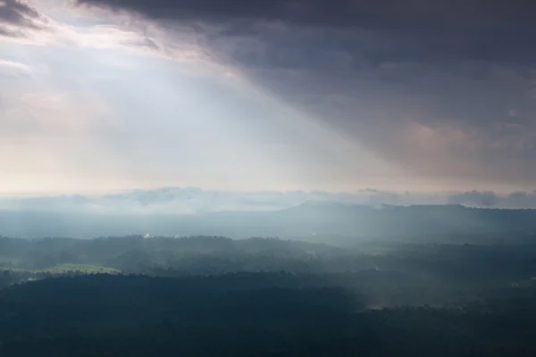 Солнечный свет светит сквозь облака в горы и лес — стоковое фото