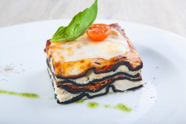 Güzel bir tabakta İtalyan lazanyası, balzamik soslu ve fesleğenli.